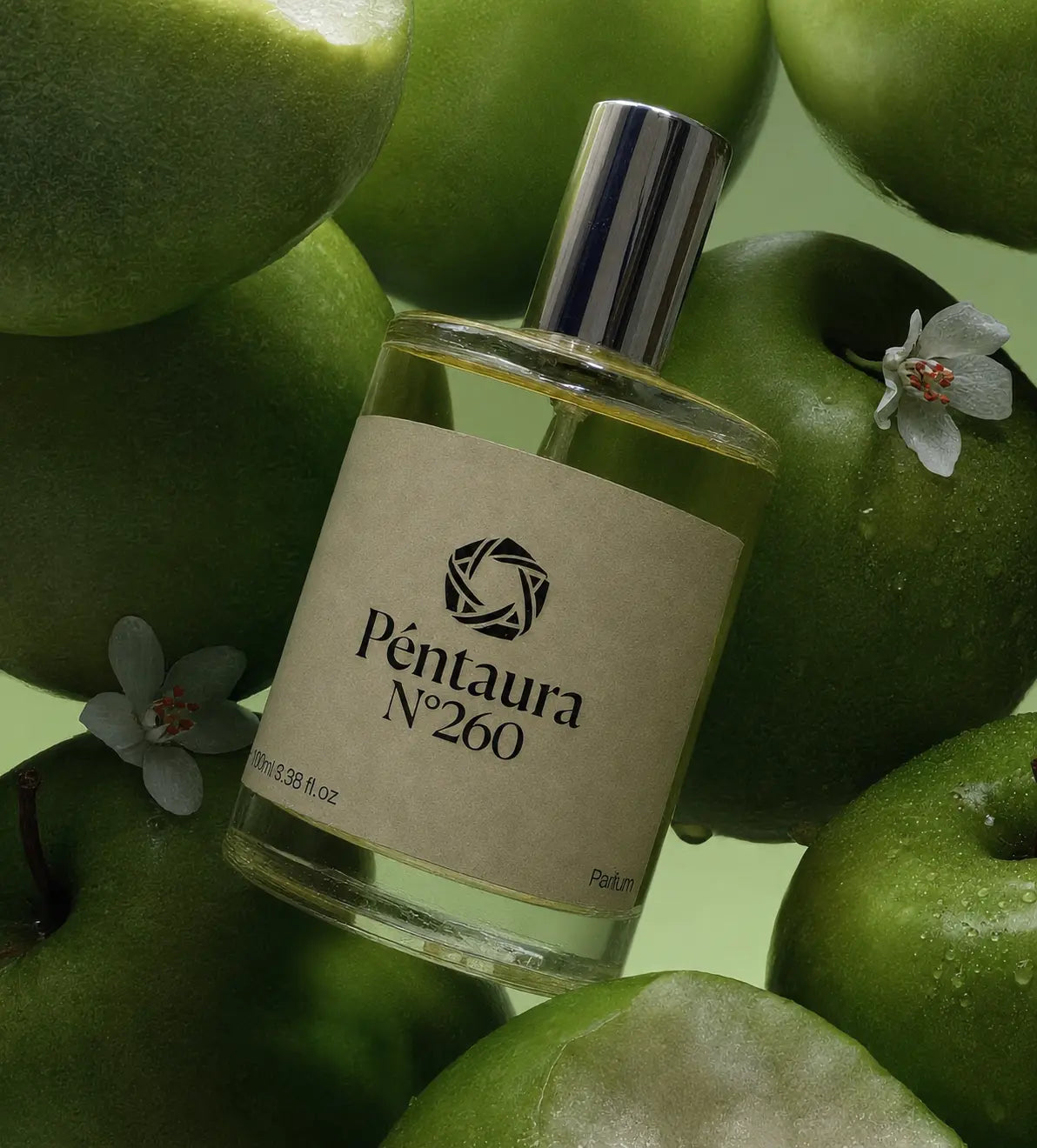 A bottle of Péntaura N°260 perfume surrounded by green apples, with a beige label and a silver cap.