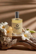 A bottle of Pentaura No. 75 perfume with a silver cap and cream-colored label, styled on a piece of driftwood with white plumeria flowers against a warm brown background with leaf shadows.