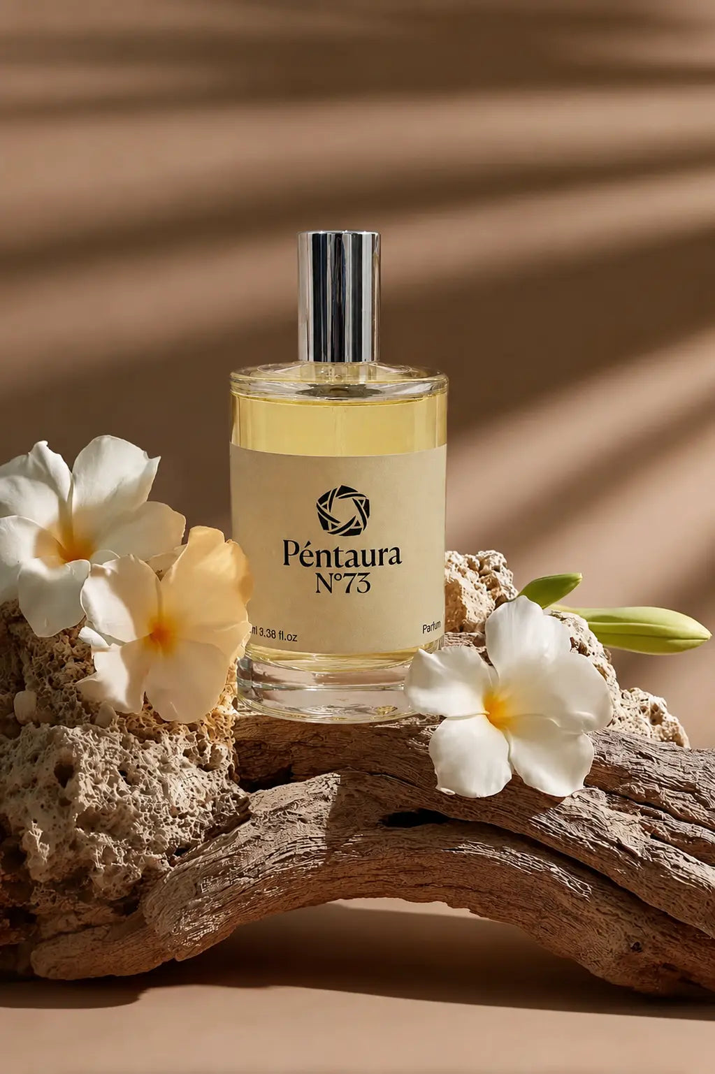 A bottle of Pentaura No. 75 perfume with a silver cap and cream-colored label, styled on a piece of driftwood with white plumeria flowers against a warm brown background with leaf shadows.