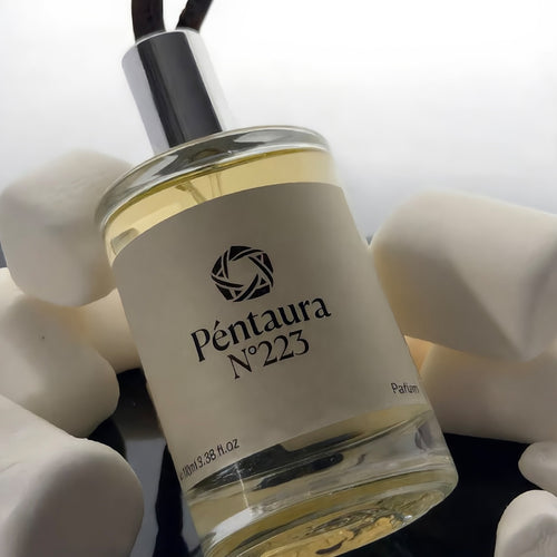 A clear glass reed diffuser bottle filled with pale yellow liquid, featuring a cream label with the brand name 'Péntaura N°223' and a black geometric logo. The diffuser is styled among smooth white stones on a reflective dark surface.