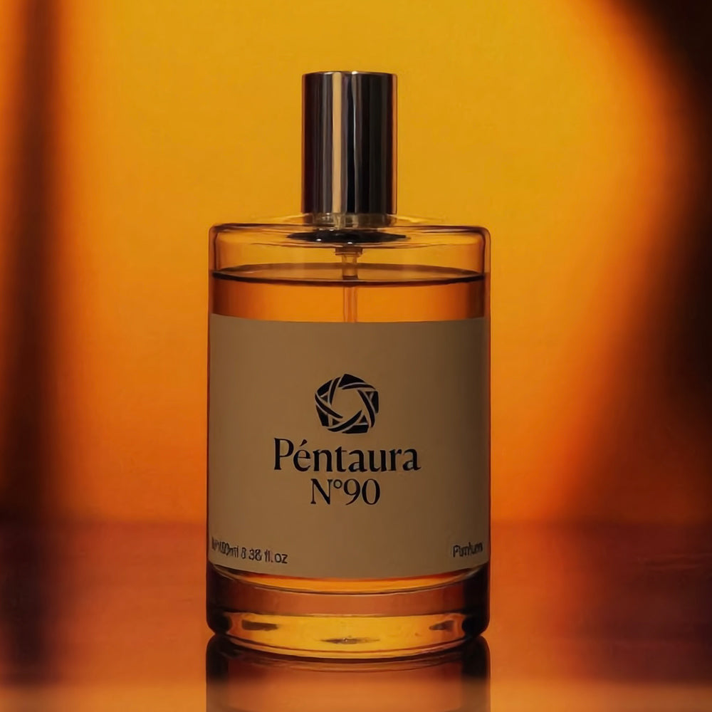 Péntaura N°90 perfume bottle with amber liquid and a white label, set against a warm orange gradient background.